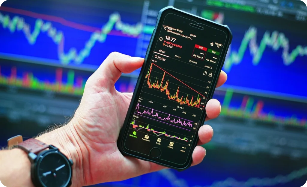 Main tenant un téléphone affichant la bourse, avec un graphique en arrière-plan, illustrant l’investissement boursier CGPM+ : diversification, rendement, dividendes.